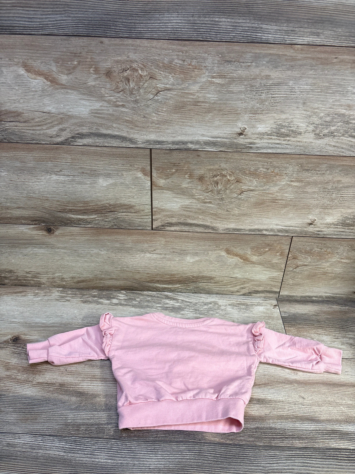 Back view of Jessica Simpson toddler pink sweatshirt size 12 months showcasing ruffle shoulder details laid flat on wood background