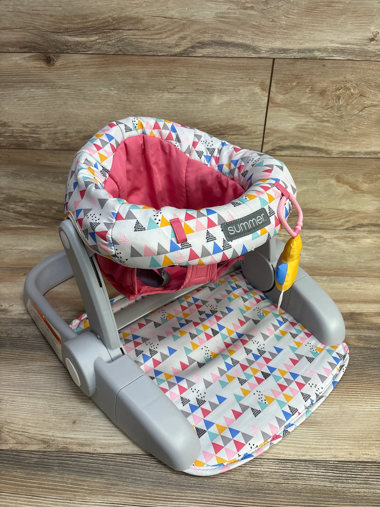 Colorful baby floor seat with geometric triangle print and pink padded interior on wooden background