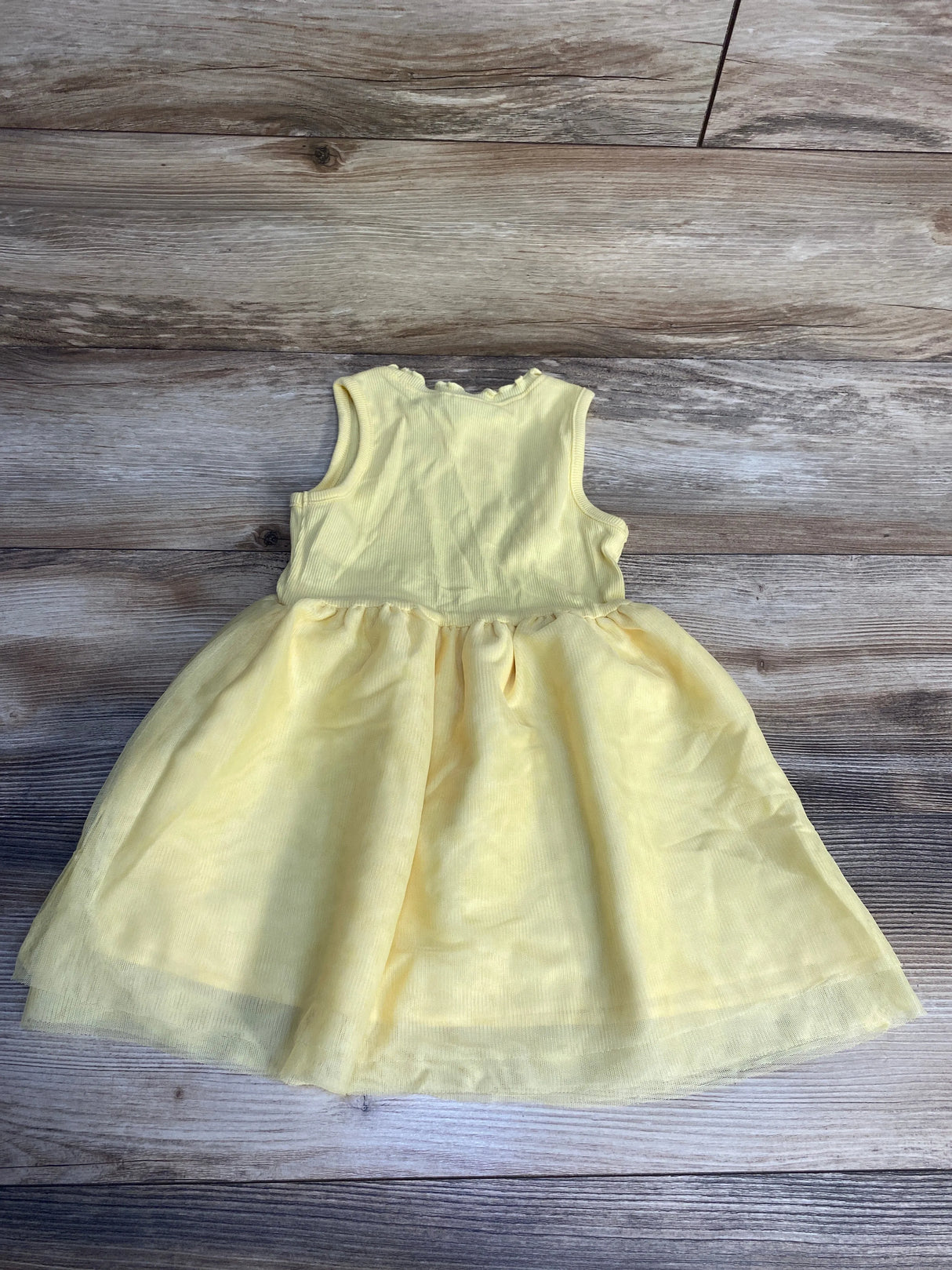 Yellow sleeveless toddler dress with tulle skirt on wood background