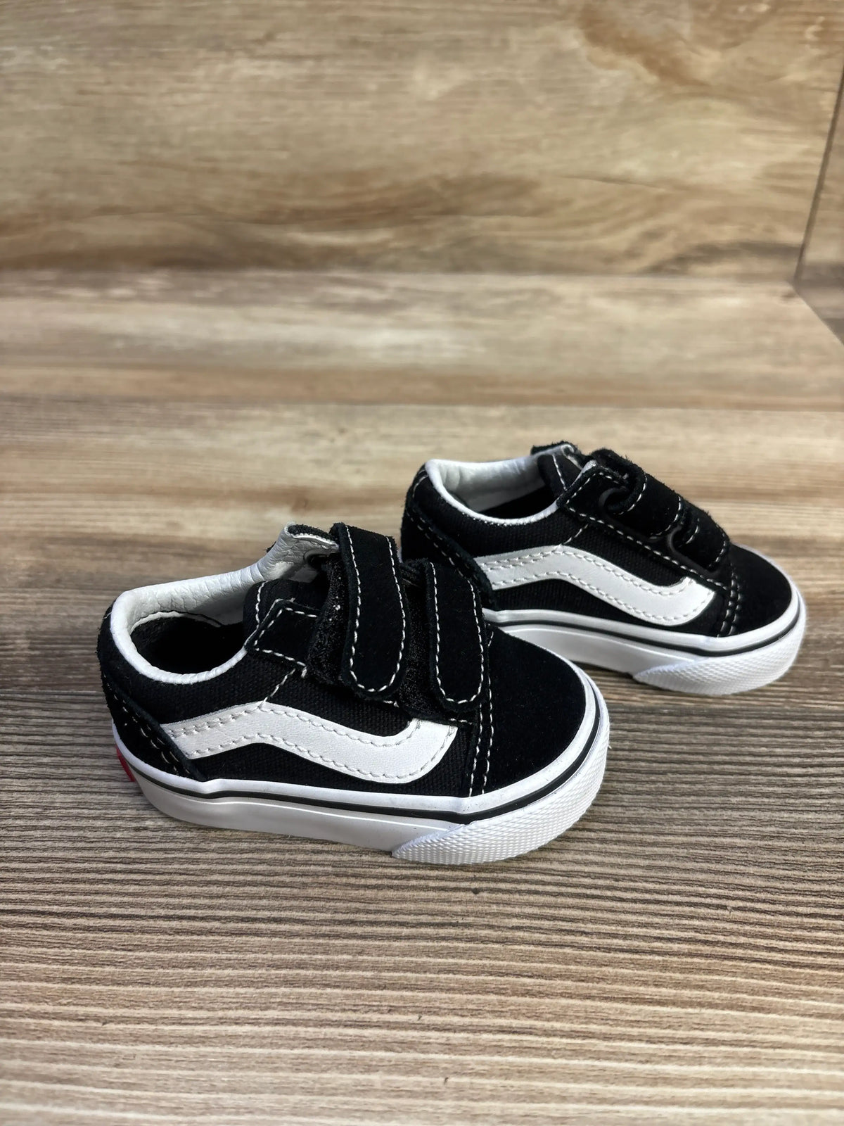 Angled view of black Vans Old Skool V sneakers in toddler size 2C showcasing hook-and-loop straps and white side stripes on a wood-grain floor