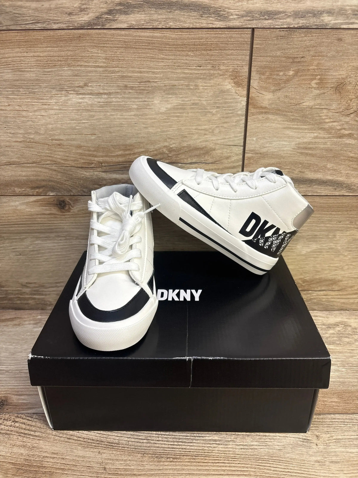 Side and front view of white DKNY high-top girls sneakers with black toe trim and DKNY heel logo on black shoebox