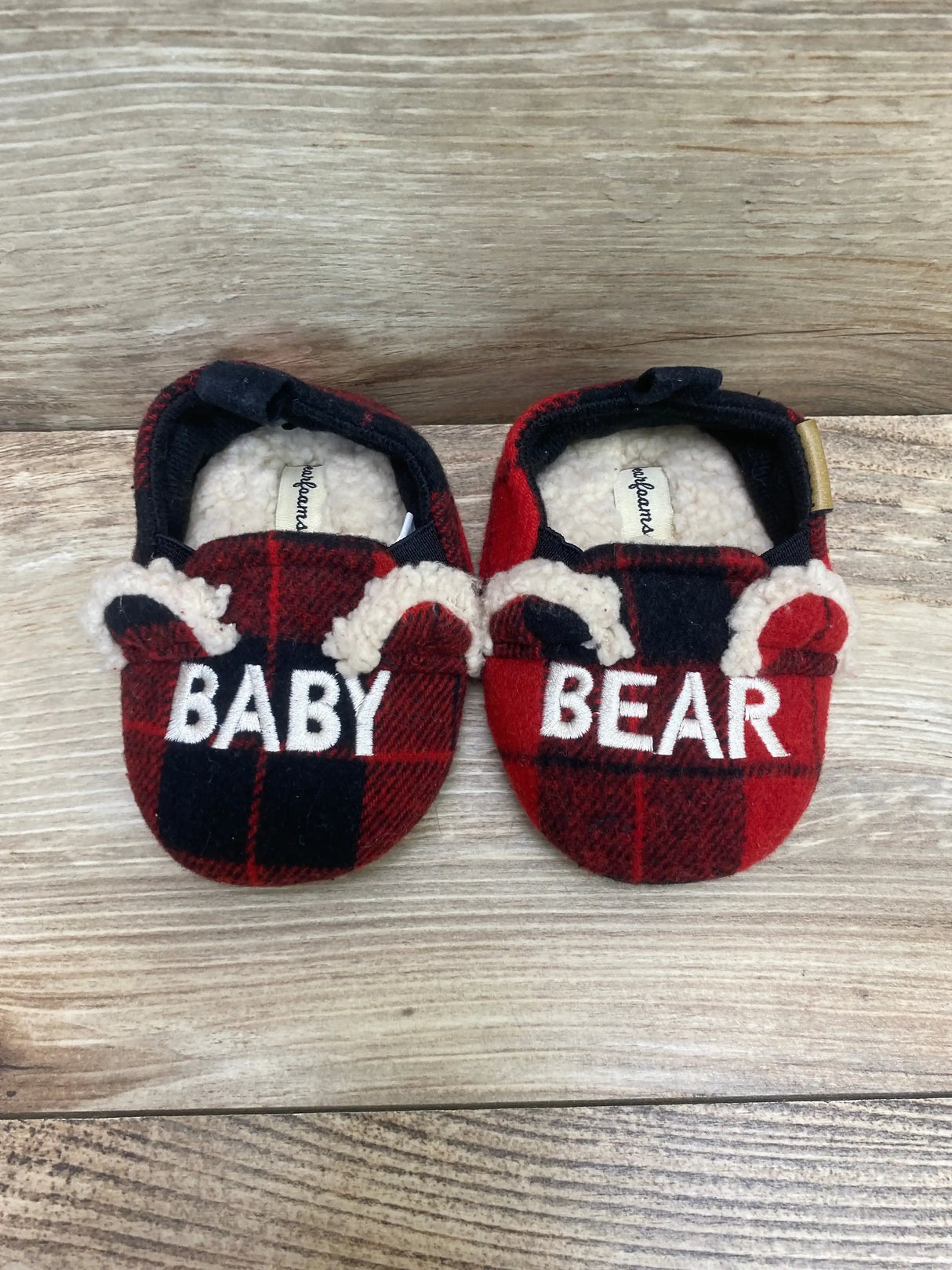 Overhead of baby bear slippers 4C showing red and black plaid, embroidered BABY and BEAR, shearling ears on light wood