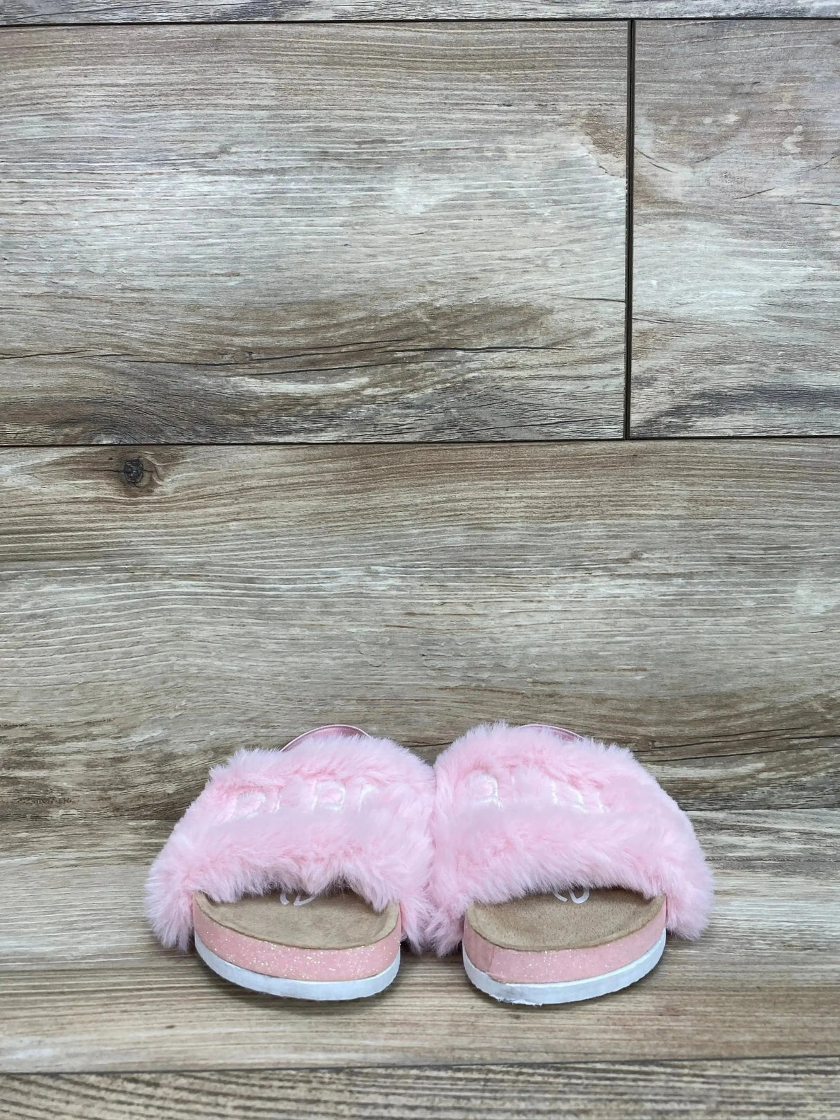 Front view of toddler pink faux-fur slide sandals with fluffy strap and sparkly sole on wood floor