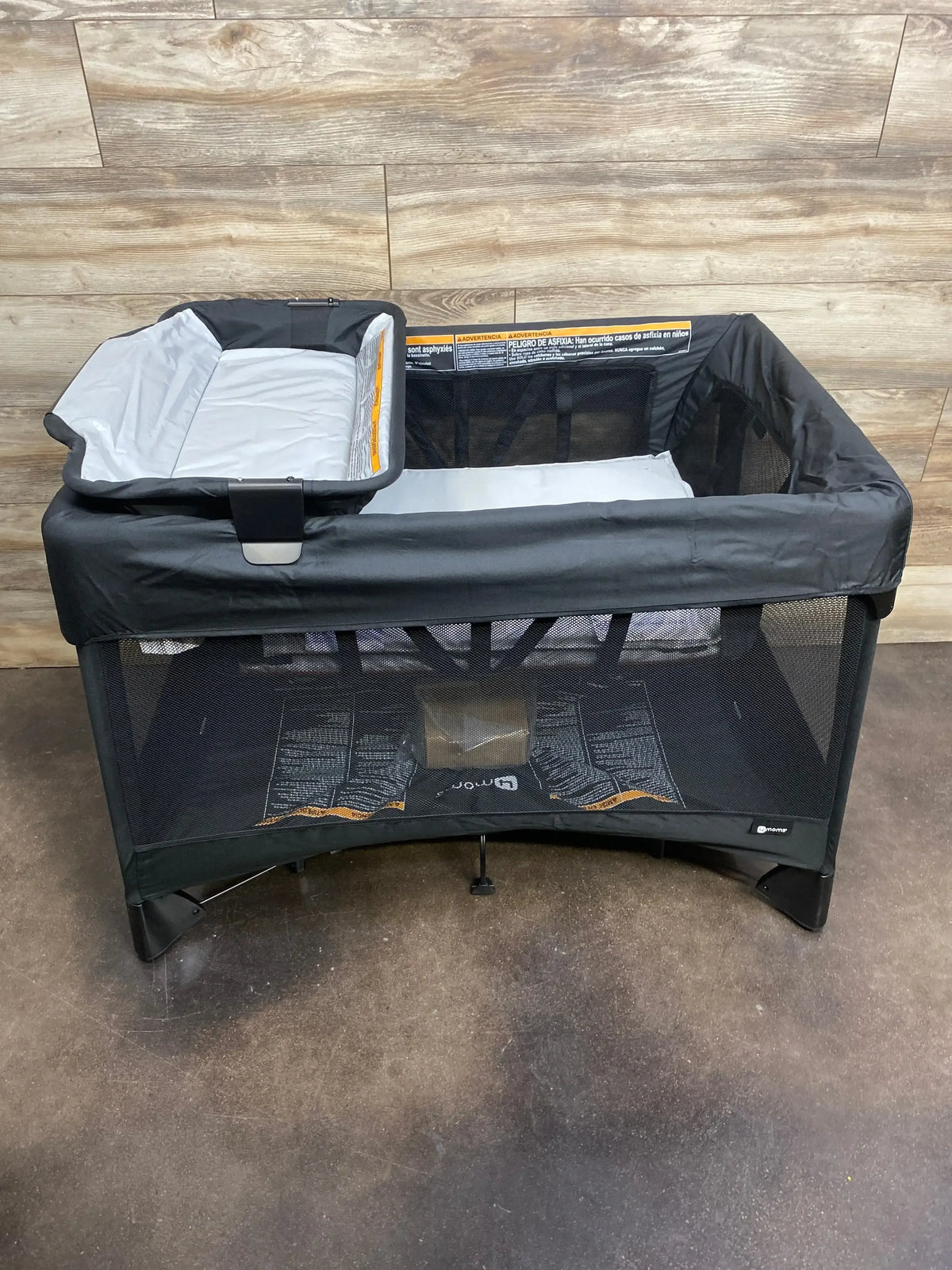 Front view of 4moms Breeze Plus playard showcasing attached changing tray and mesh sides with wood-plank wall background