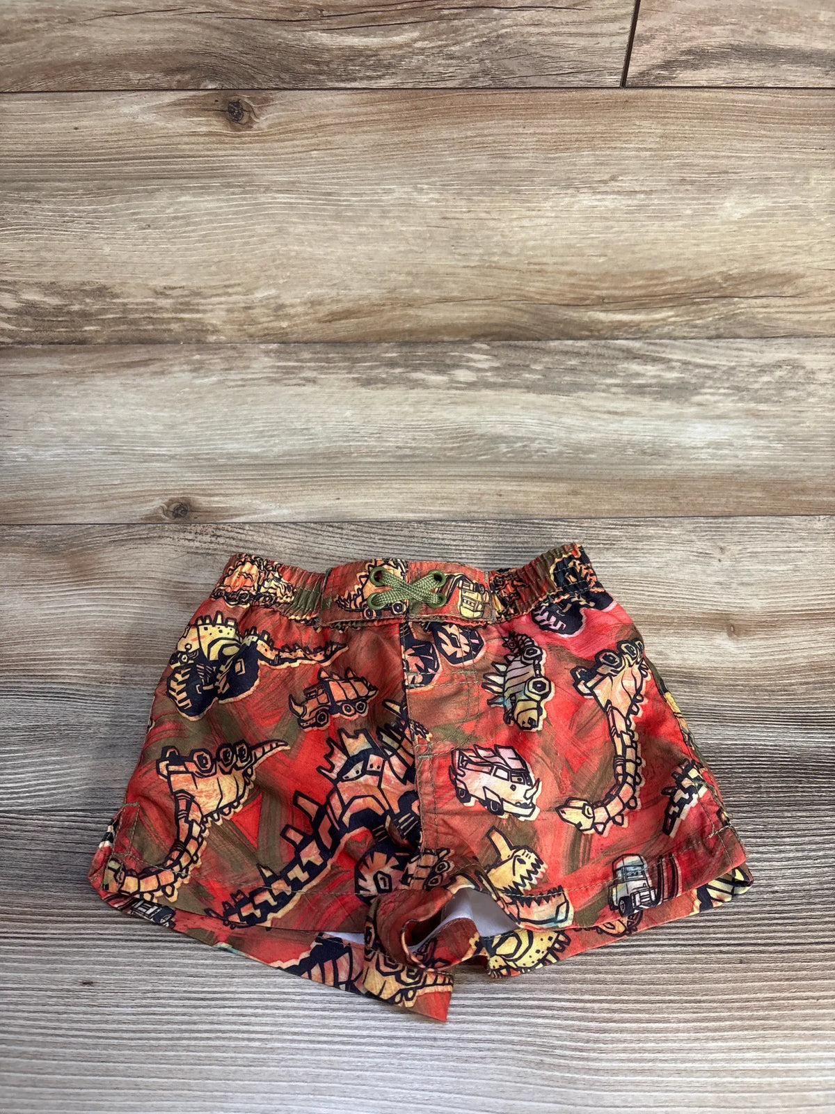 Front view of Disney Pixar Cars swim trunks showcasing red character graphics and elastic waistband on a wood surface