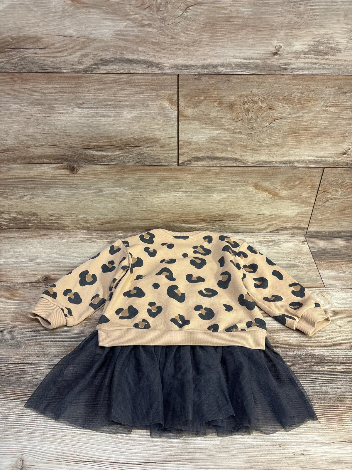 Front view of H and M leopard tulle skirt sweatshirt dress showing beige leopard print top and black tulle skirt on wood flooring