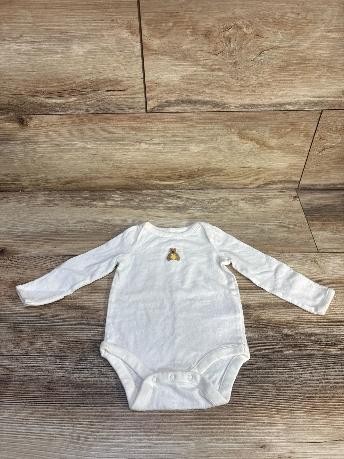 Front view of Baby Gap white long sleeve bodysuit showcasing bear chest motif and three-snap closure on a wood-look floor
