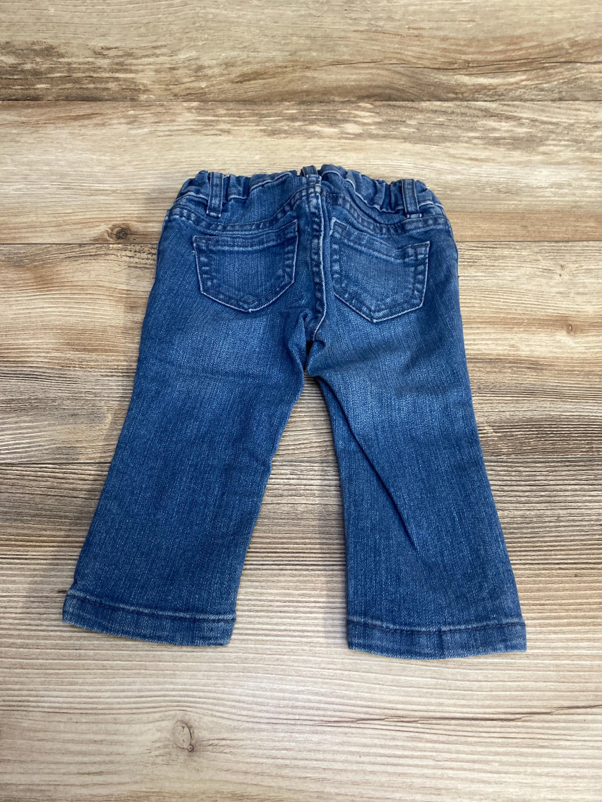 Back view of children's blue super skinny jeans showing elastic waistband and back pockets on wooden floor
