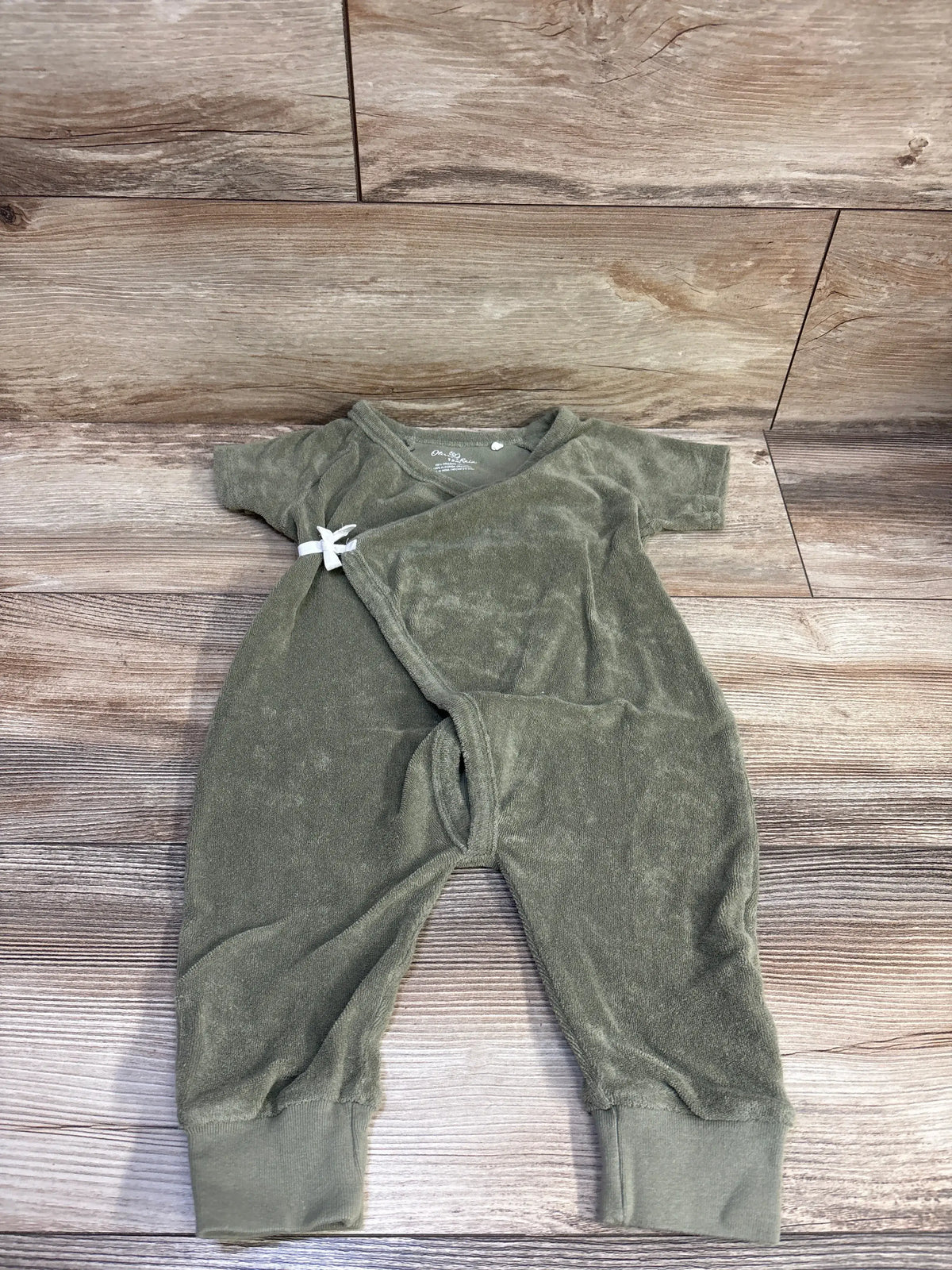 Flat lay of Oliver & Rain green terry cloth jumpsuit (12 months) showing short sleeves, kimono wrap with white tie and ribbed ankle cuffs on wood background