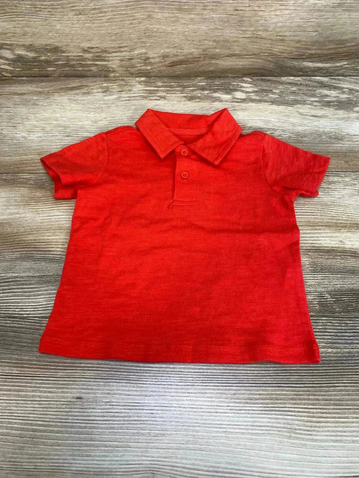 Flat lay of red baby polo shirt 6-9 months with short sleeves and two-button placket on light wood background