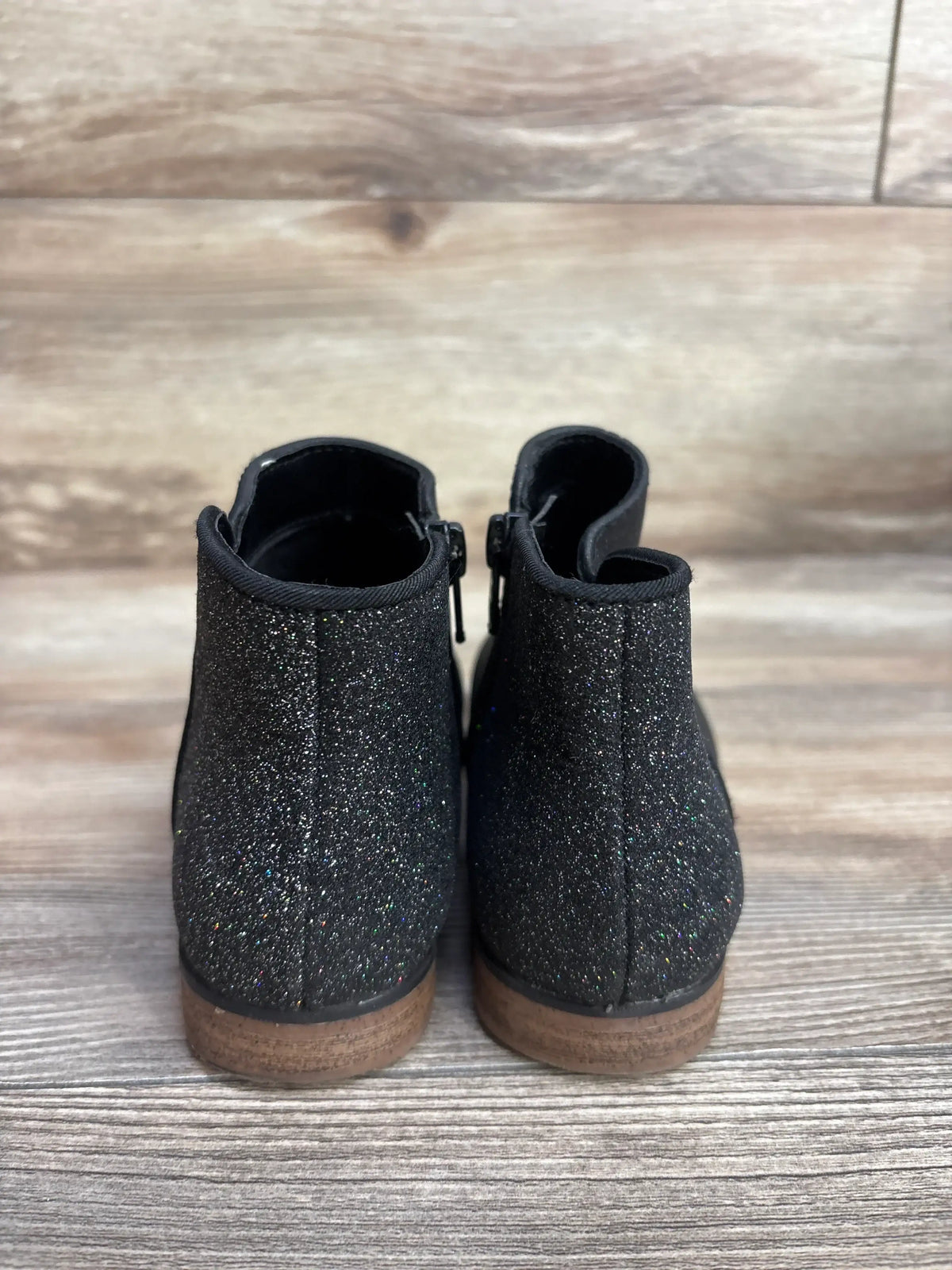 Rear view of Cat & Jack Glitter Ankle Boots showcasing sparkly black glitter upper and brown stacked soles with wood background