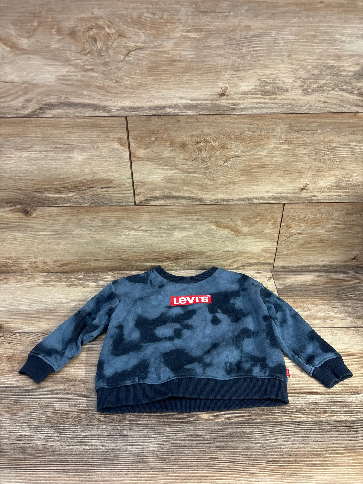 Flat lay of Levi’s toddler blue tie-dye pullover sweatshirt with red logo on chest on wood floor background