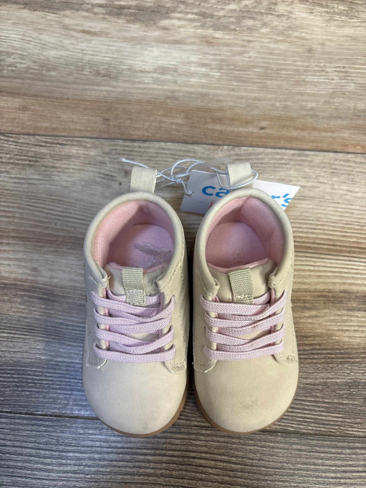 Beige baby shoes with pink laces on wood floor, gently used toddler footwear