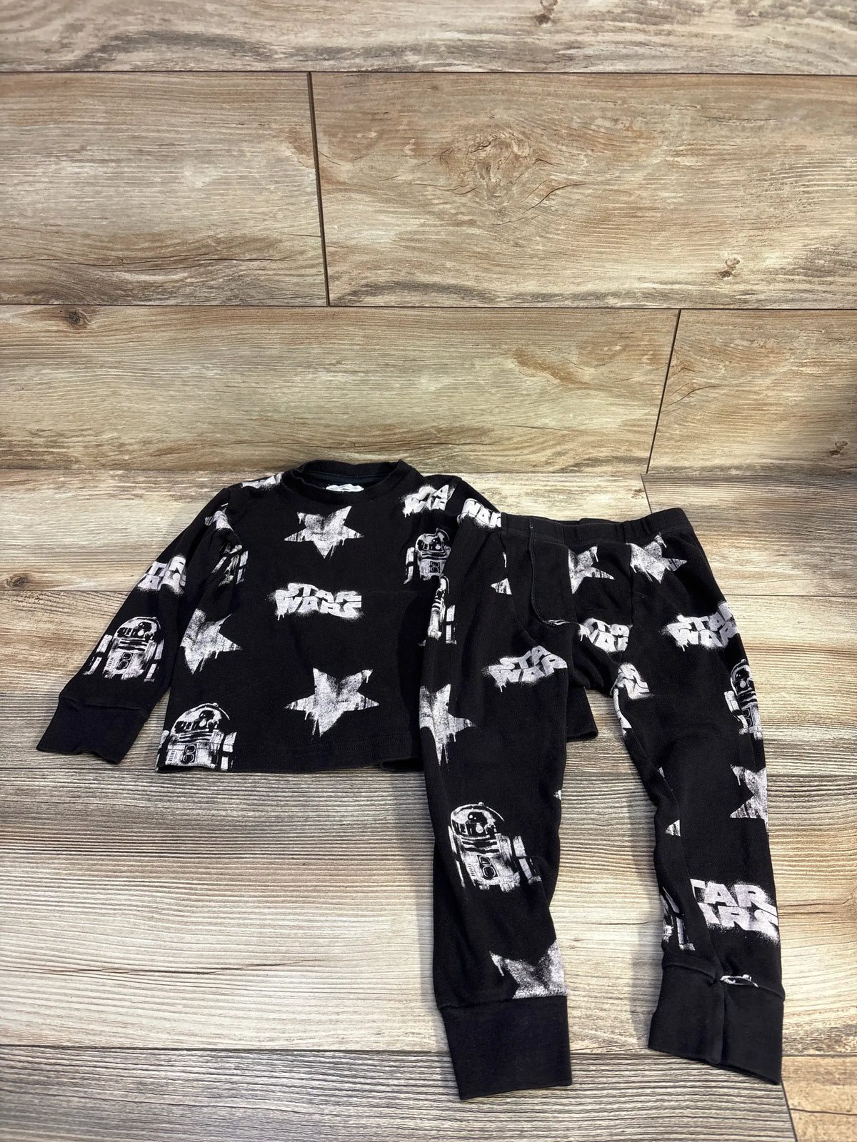 Flat lay of toddler black 2-piece pajama set showcasing white R2-D2 and star prints on wood floor