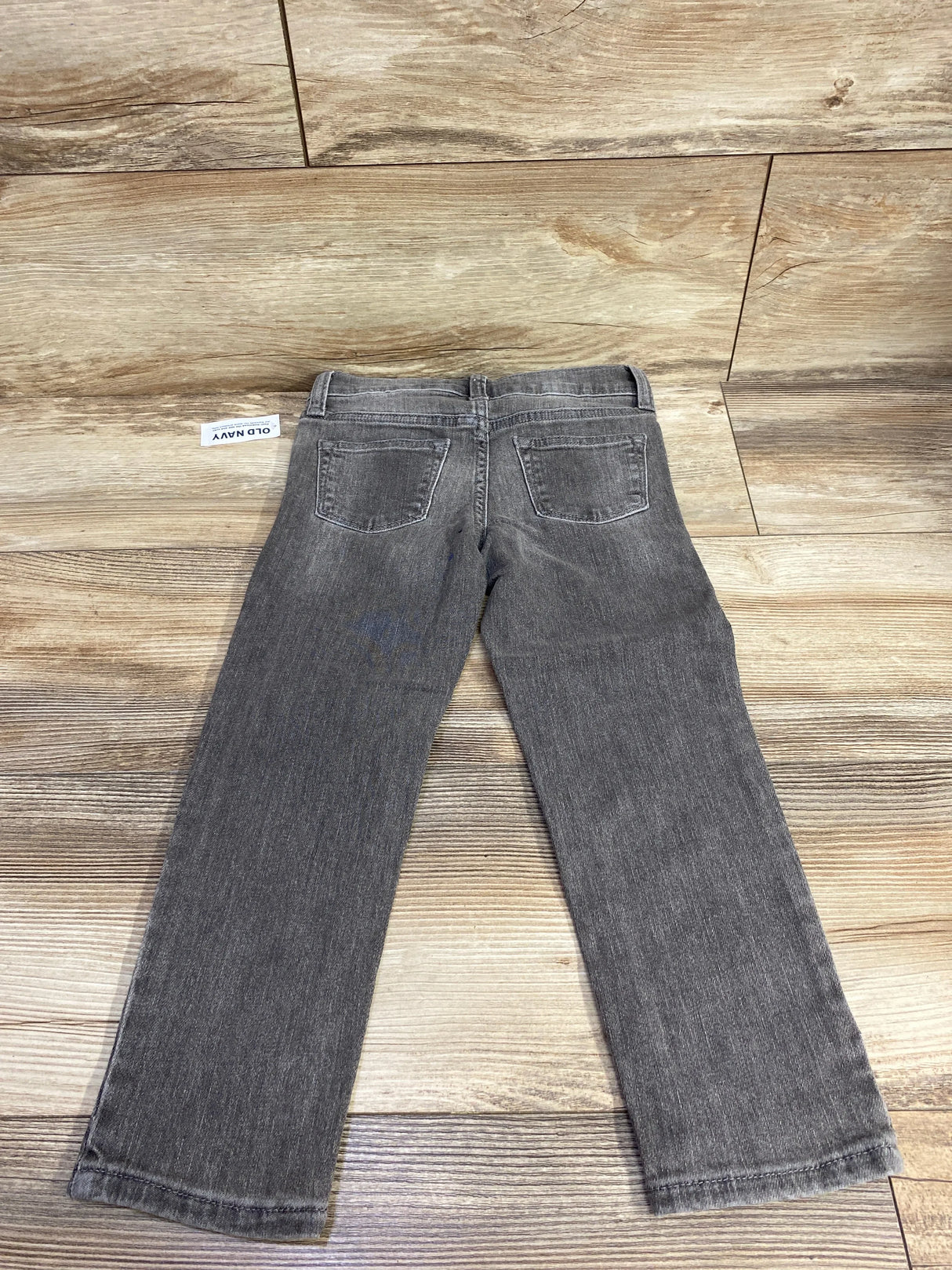 Gray kids' jeans with back pockets displayed flat on wooden background