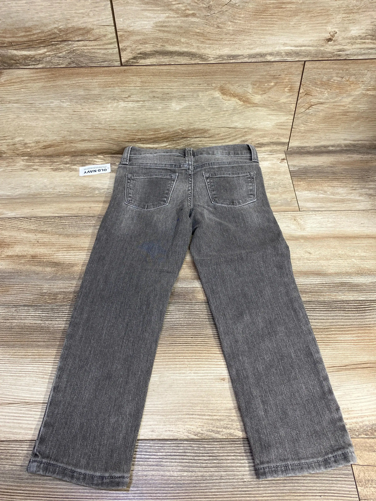Back view of new Old Navy 360 Stretch skinny jeans showcasing grey wash back pockets and hangtag on wood plank floor