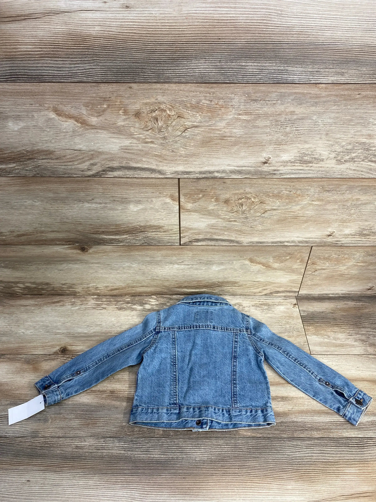 Back view of a light blue denim jacket with long sleeves on wooden floor background