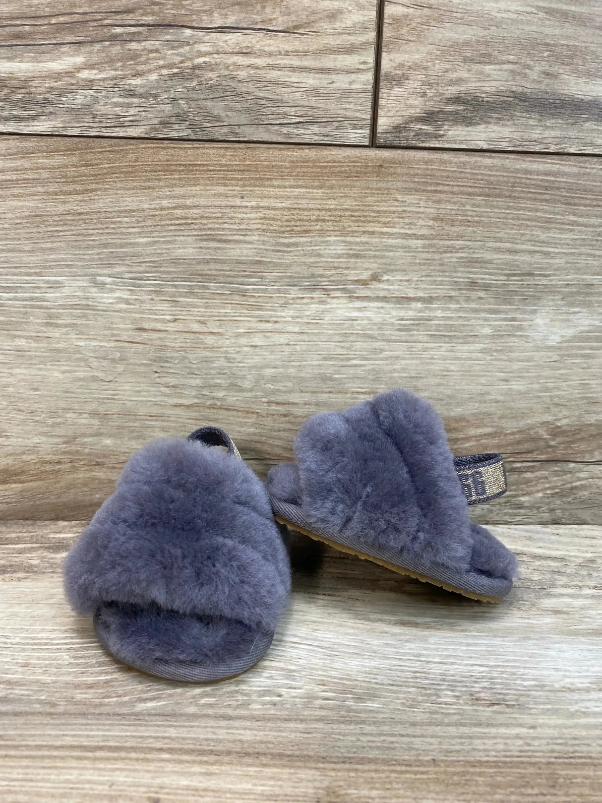 Front three-quarter view of toddler UGG Fluff Yeah slide in grey shearling with elastic logo heel strap on wood background