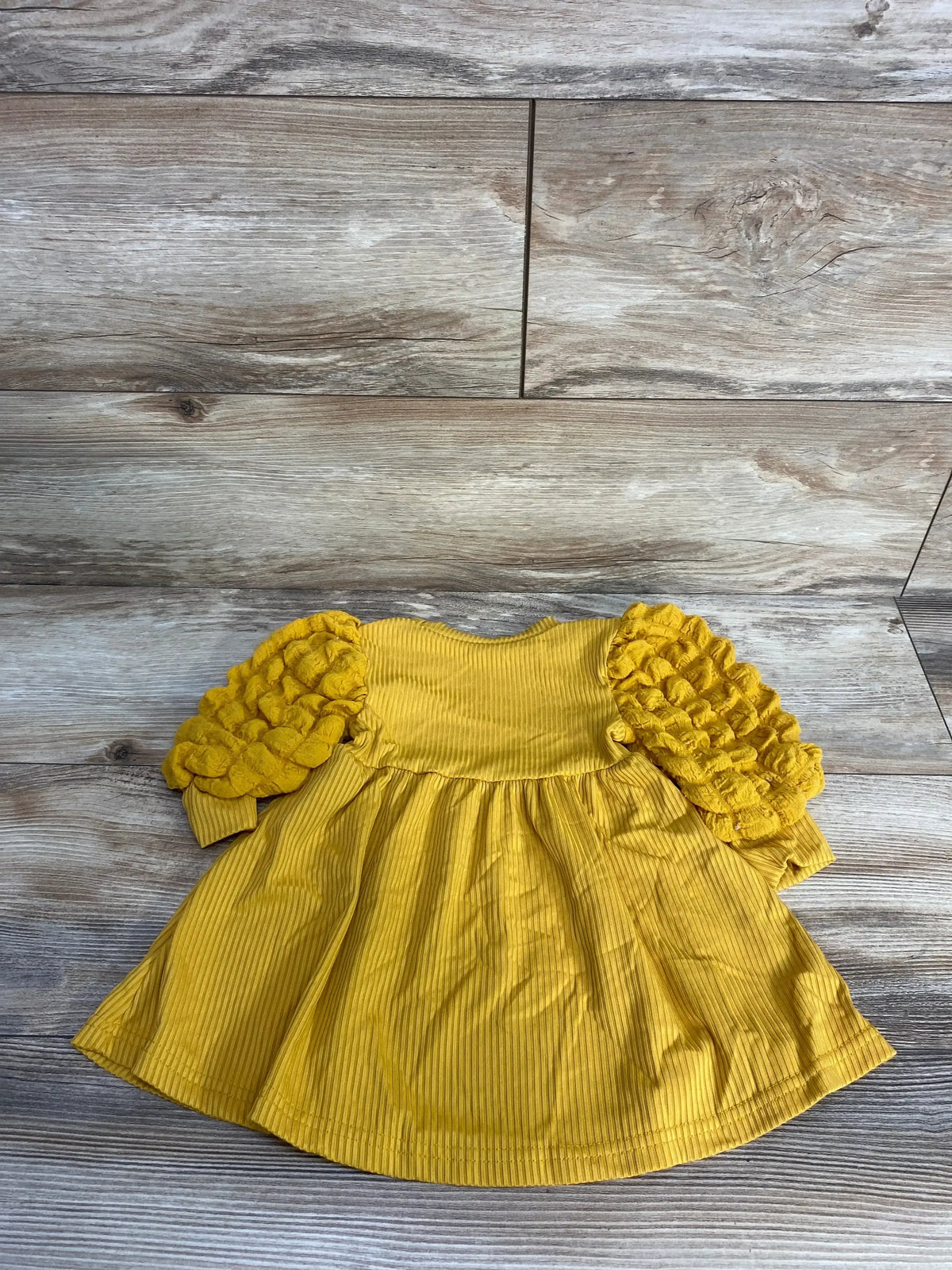 Mustard yellow baby dress with ruffle sleeves on wood background