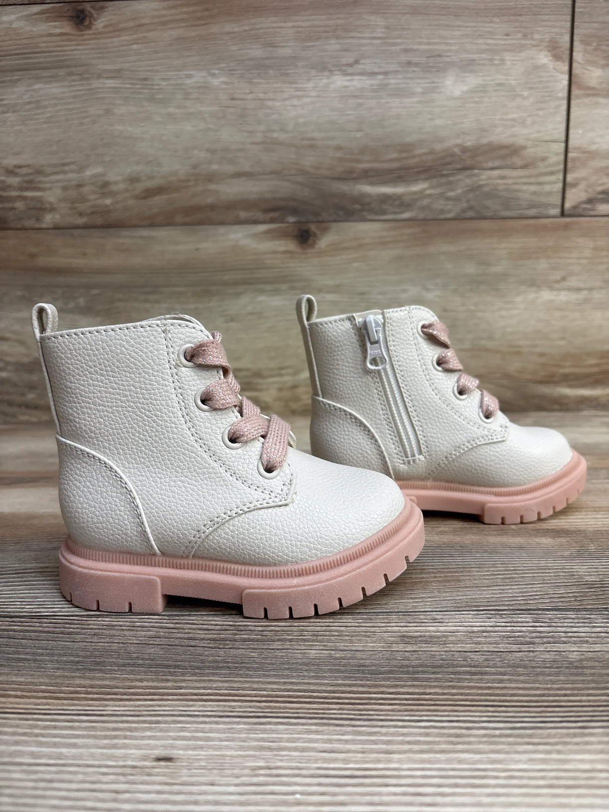Pair of white toddler boots with pink soles and laces on a wooden floor background