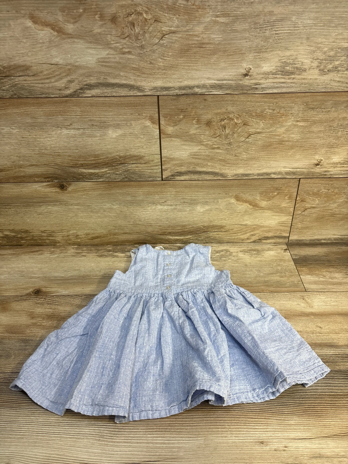 Flat lay of H&M blue linen-blend baby dress showing sleeveless bodice and gathered skirt, size 12-18m on wood floor