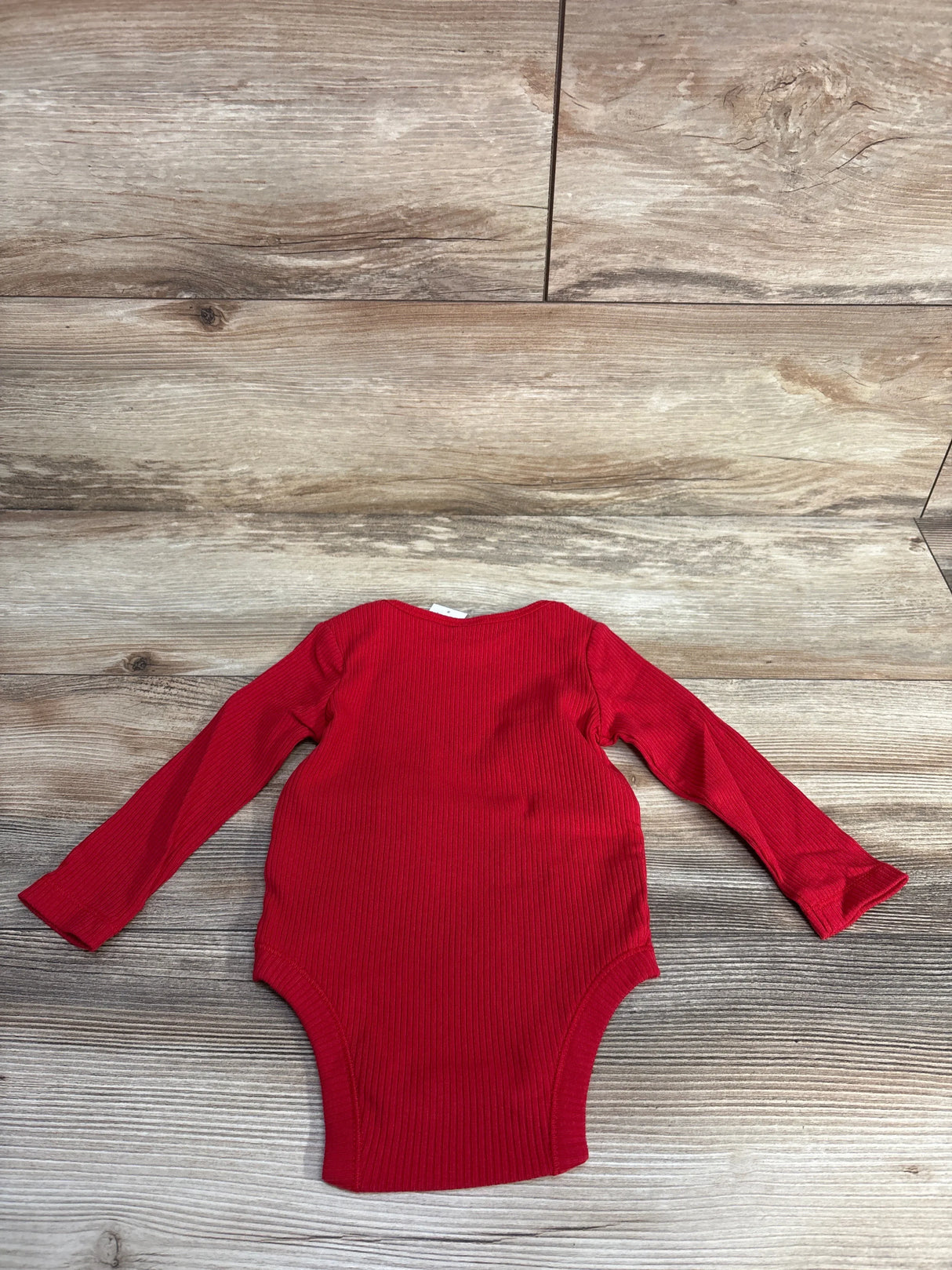 Red long sleeve baby bodysuit on wooden floor, ribbed cotton fabric