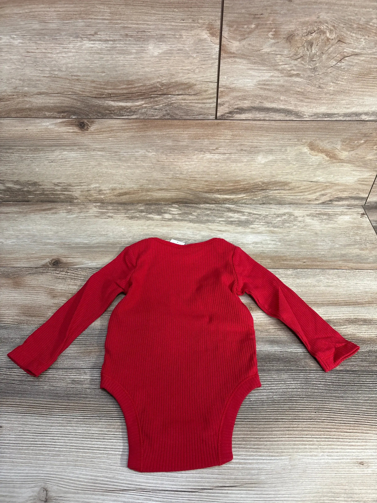 Red long sleeve baby bodysuit on wooden floor, ribbed cotton fabric
