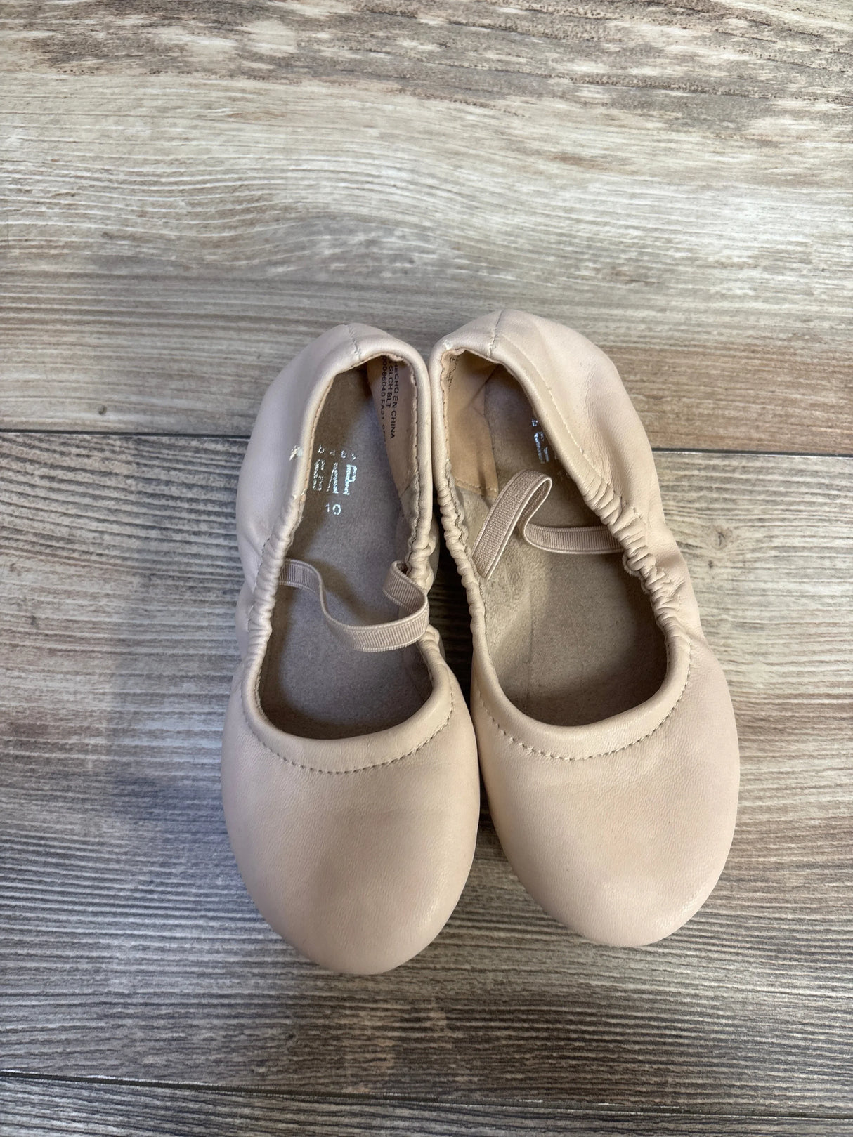 Pair of light beige toddler ballet flats with elastic straps on wood background
