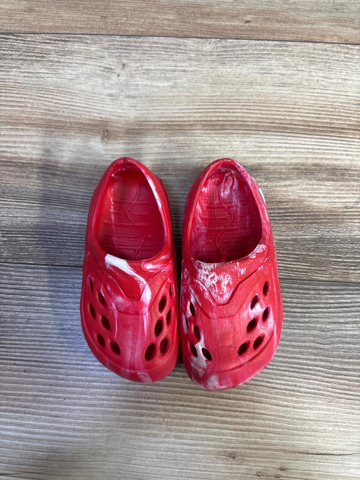 Top view of Wonder Nation USA toddler red tie-dye clogs showcasing white marbled pattern and ventilation holes on wood plank background