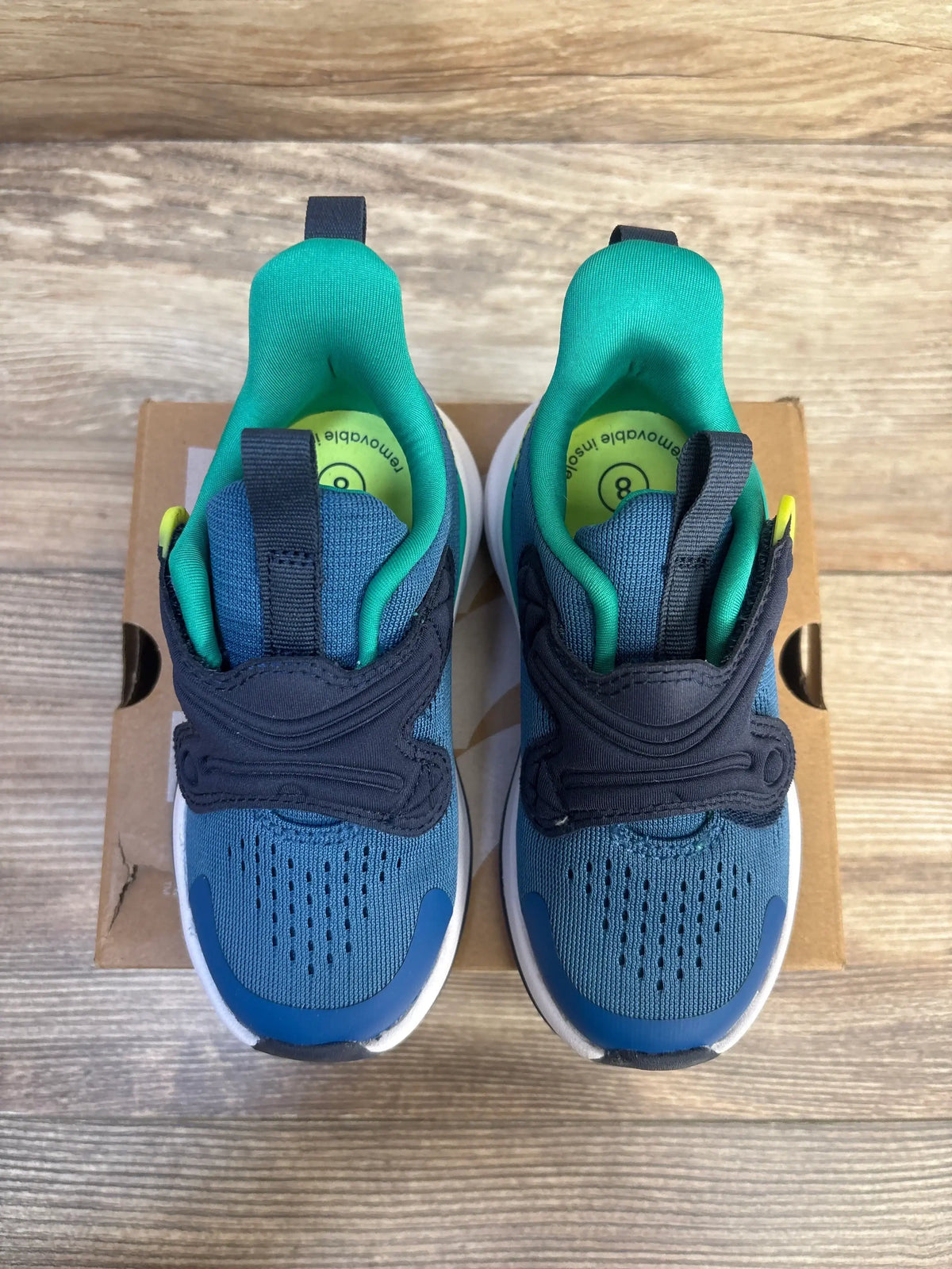 Top view of Quinn toddler sneakers size 8C with blue knit upper, navy Velcro strap and green lining on a cardboard box