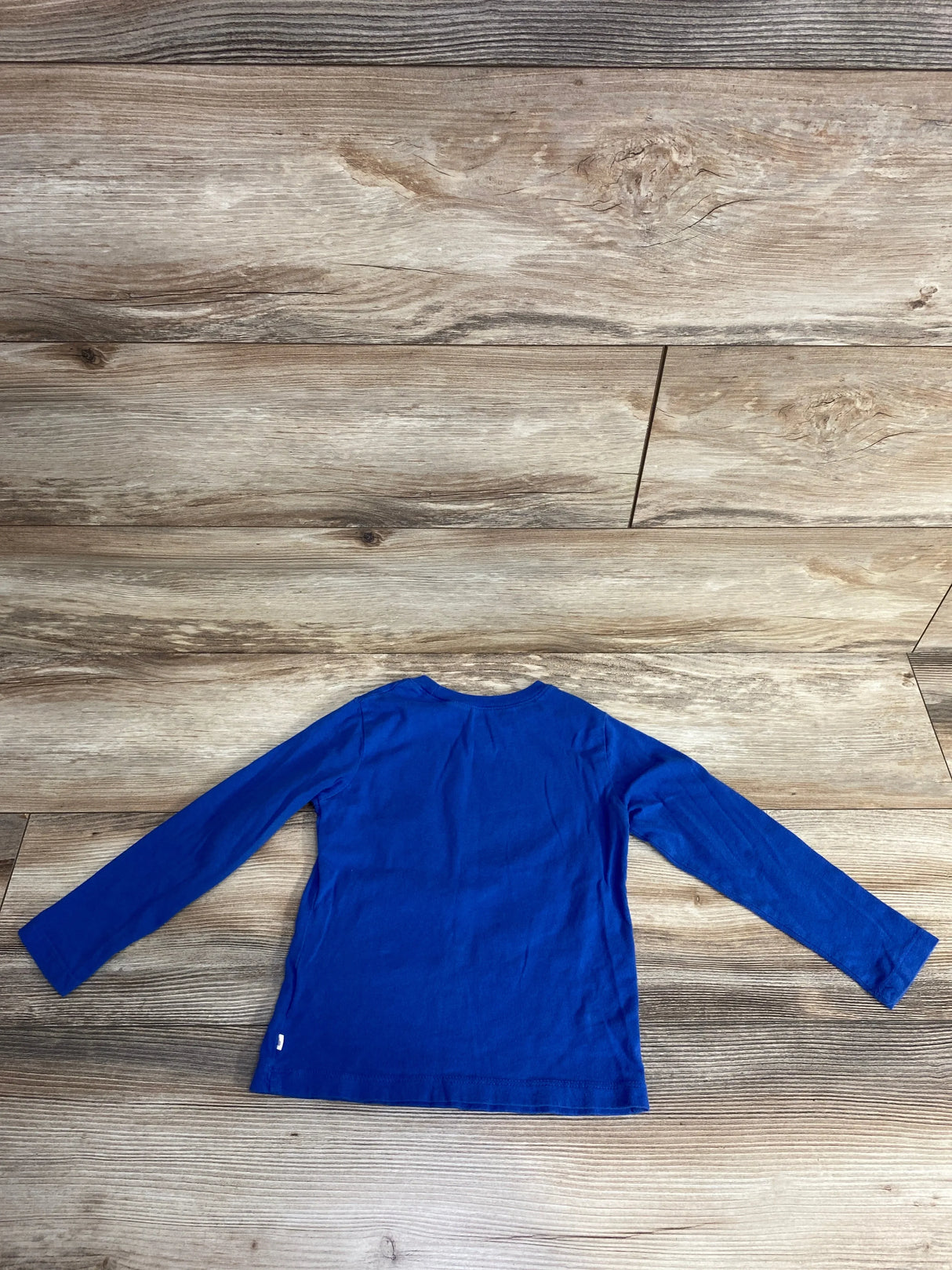 Back view of a plain long-sleeve blue shirt laid flat on wooden floor background