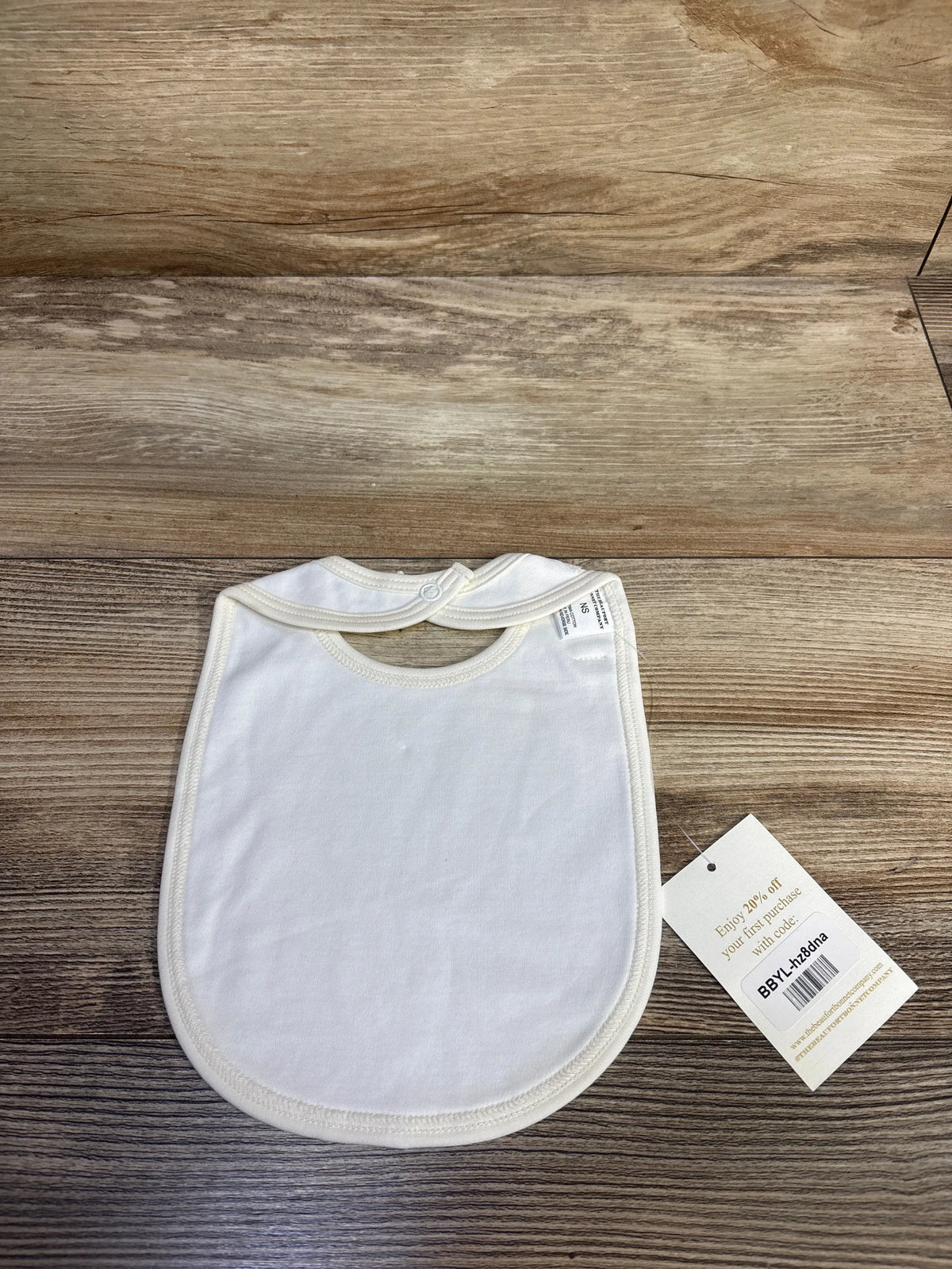 Front view of The Beaufort Bonnet Company Burp Me Bib showcasing a white bib with snap closure on a wood grain background