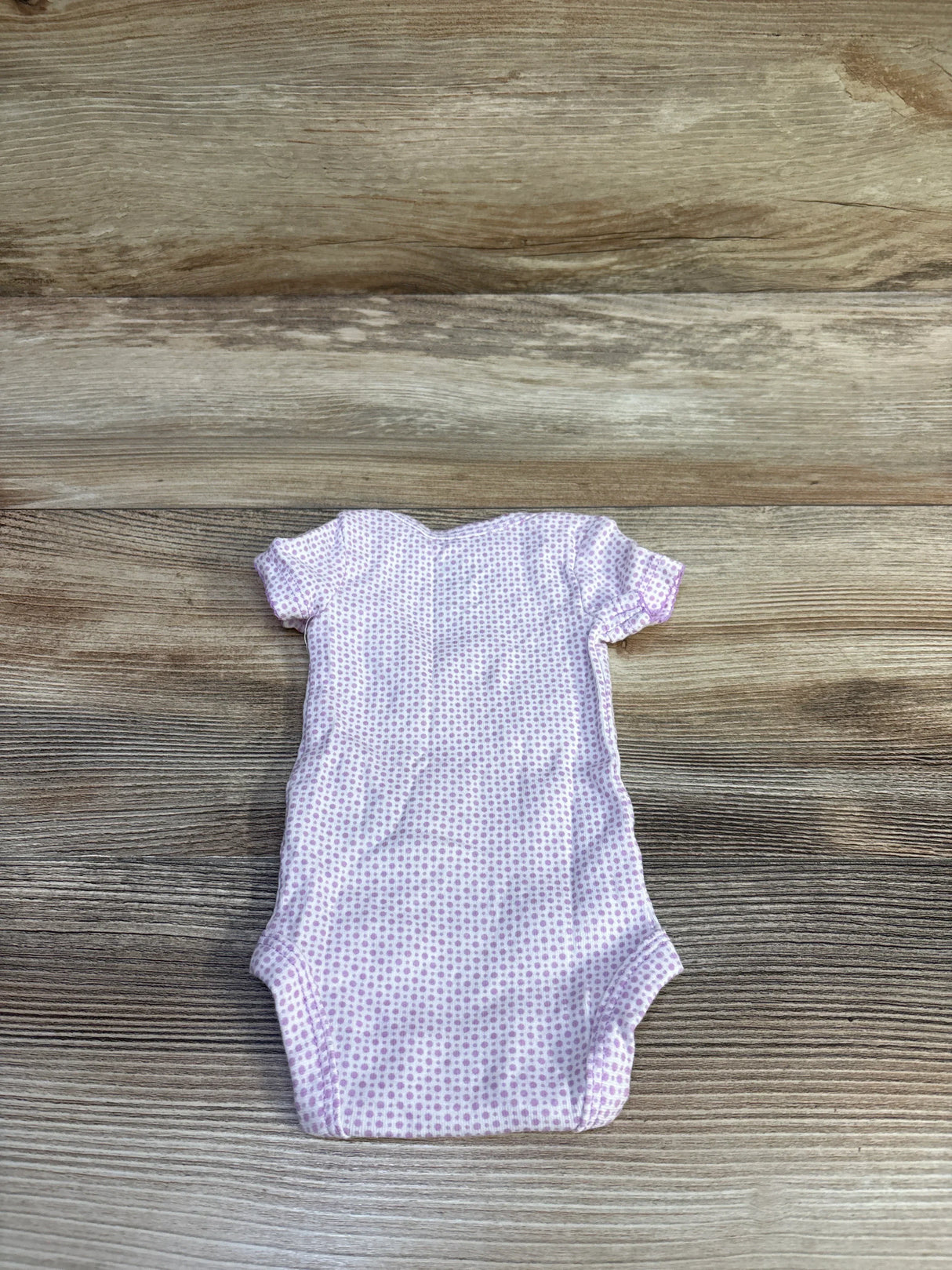 Flat lay of preemie Child of Mine Happy bodysuit showing short sleeves and light purple dot print on wood background