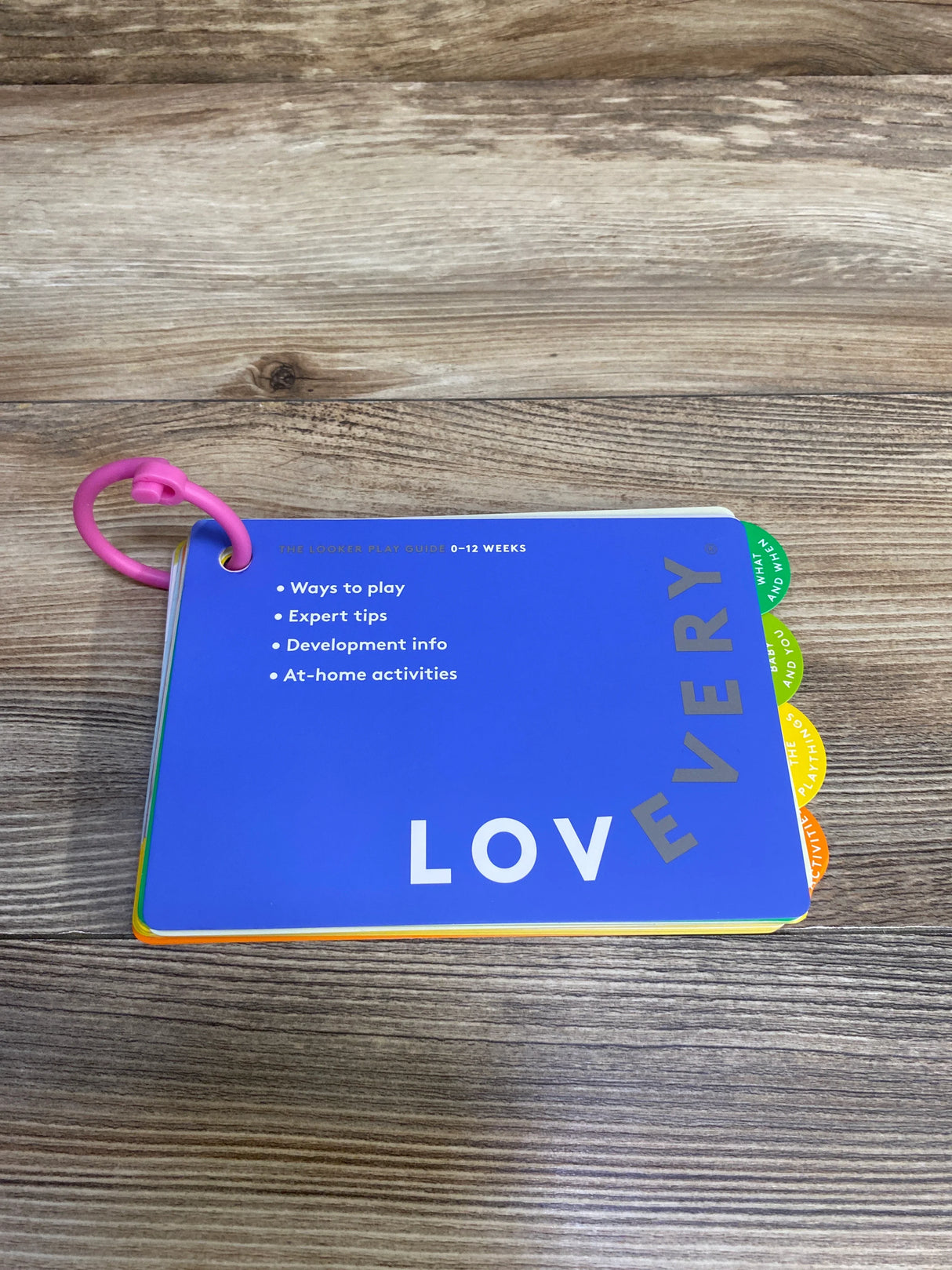 LOVEVERY Looker Play Guide for 0-12 weeks on wood table, colorful tabbed cards with pink ring
