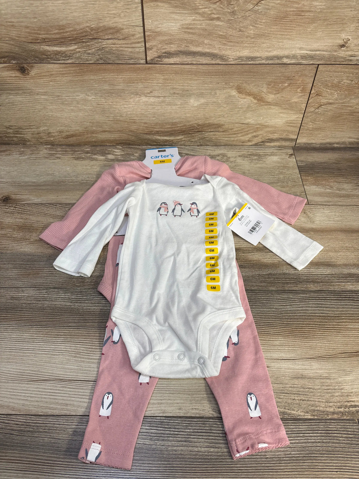 Top view of Carter’s 3-piece bodysuit set with white penguin-print and pink waffle-knit bodysuits on wood flooring