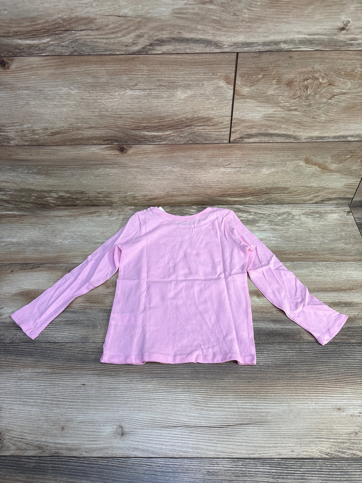Light pink long-sleeve children's shirt laid flat on a wooden floor background
