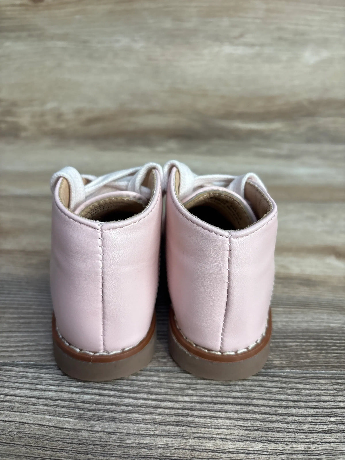 Pair of light pink leather baby shoes with white laces on wooden surface, rear view
