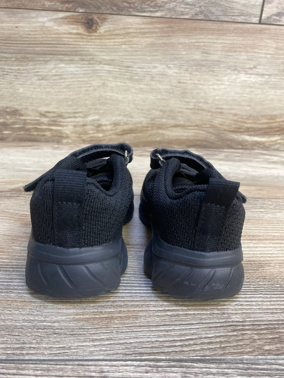 Rear view of Anlarach mesh toddler athletic shoes showcasing black knit upper, Velcro strap and heel pull tab on wood floor