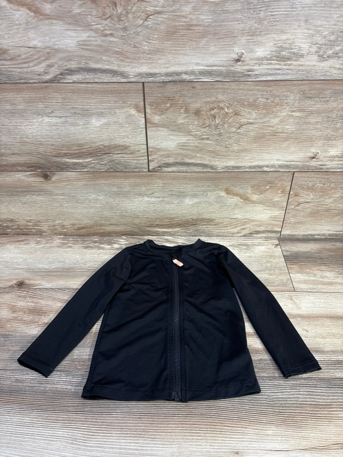 Flat lay of black Cat and Jack full zip toddler rash guard showing front zipper and long sleeves on wood floor background