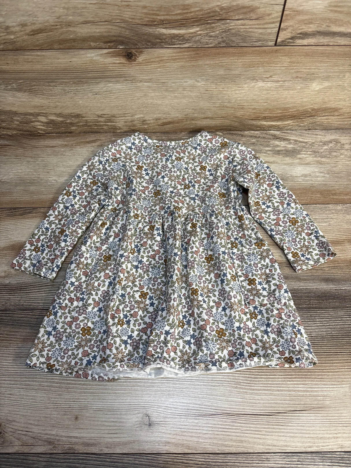 Long sleeve baby dress with colorful floral print on wood background