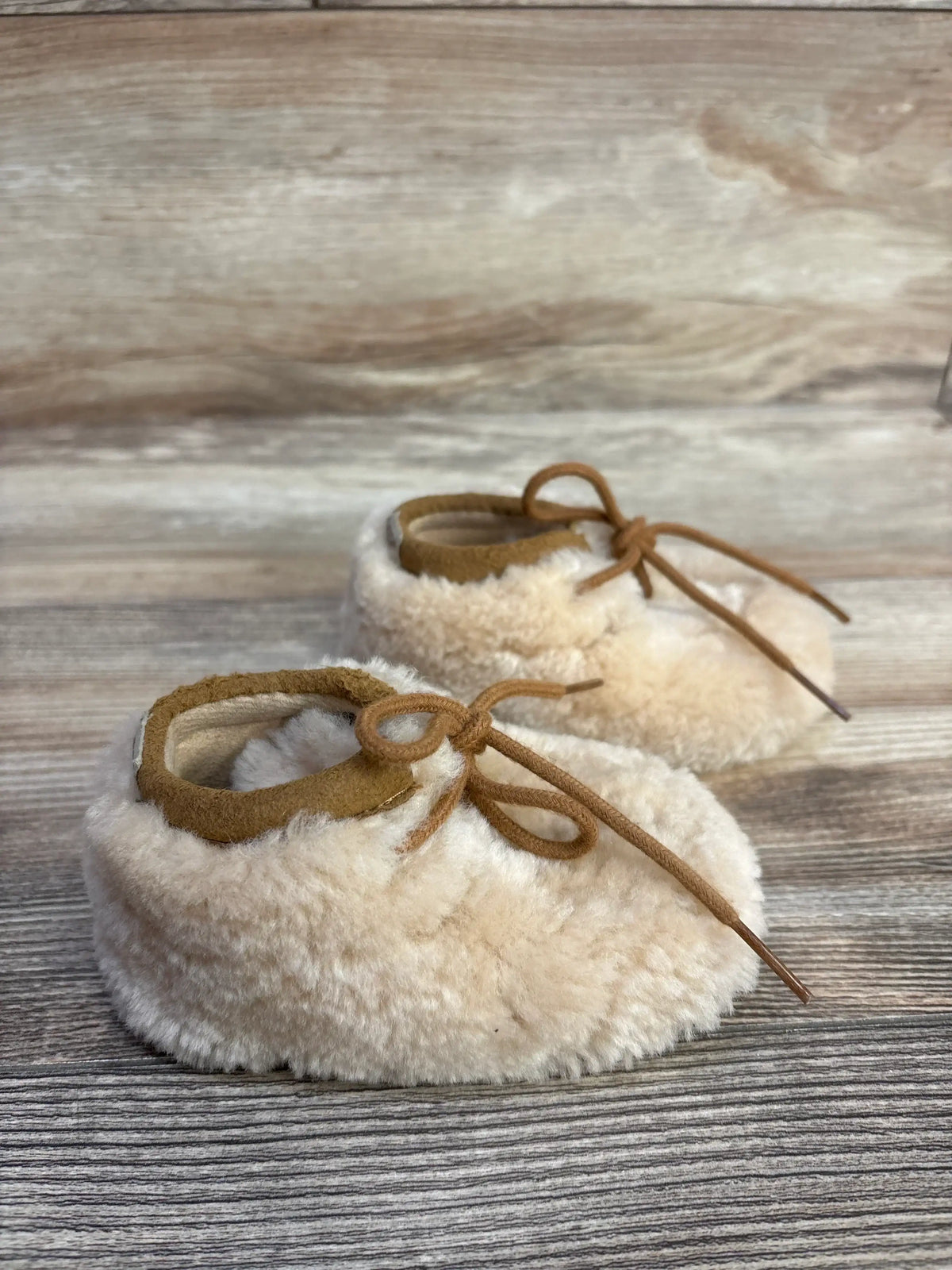 Fuzzy cream baby booties with suede laces on rustic wood background
