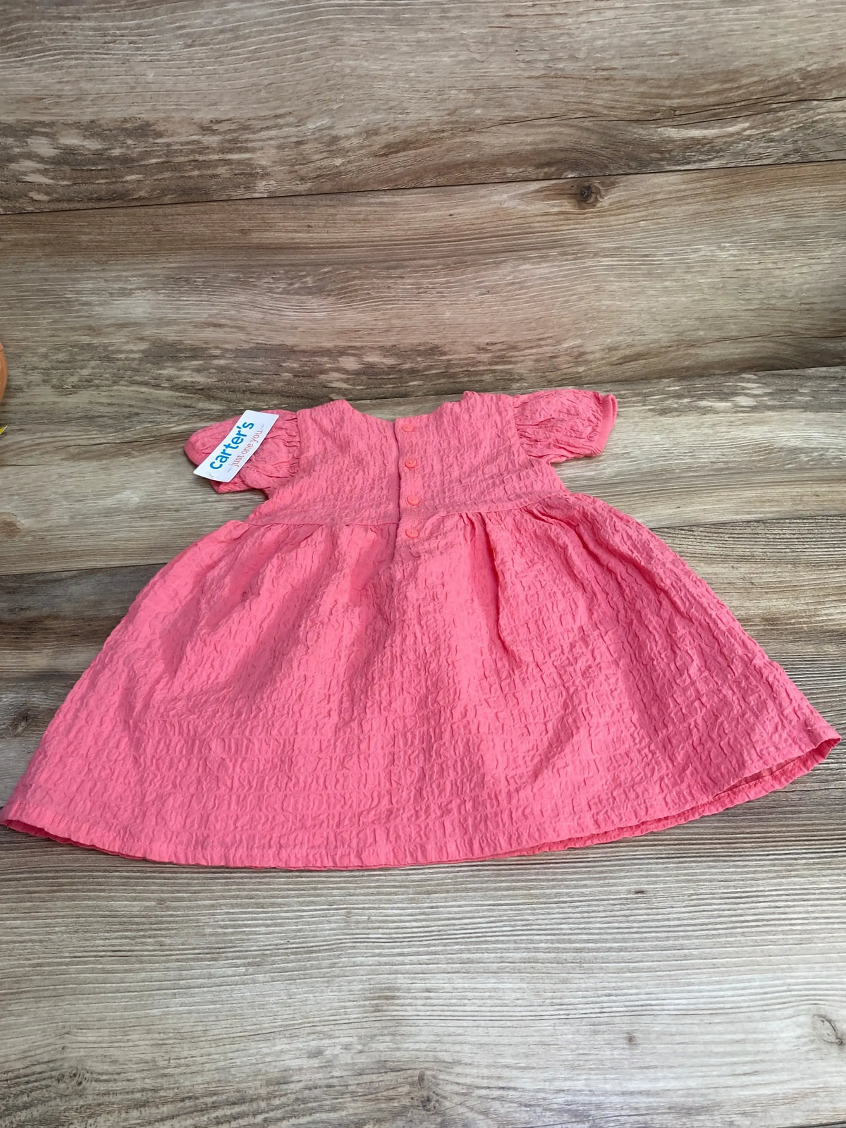 Flat lay of pink baby dress showing textured crinkle fabric, back button closure and puff sleeves on wood background