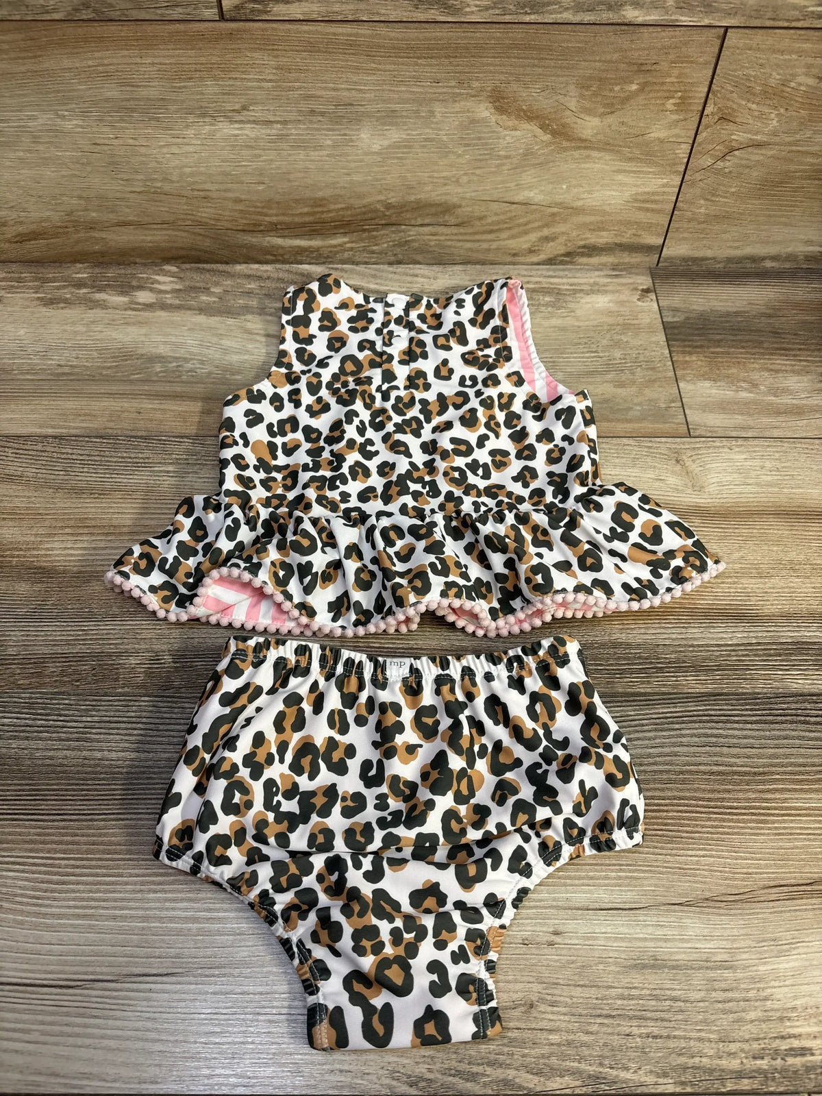 Front view of Mudpie two-piece reversible swimsuit set showcasing leopard print, pom-trimmed peplum flounce and matching bottoms