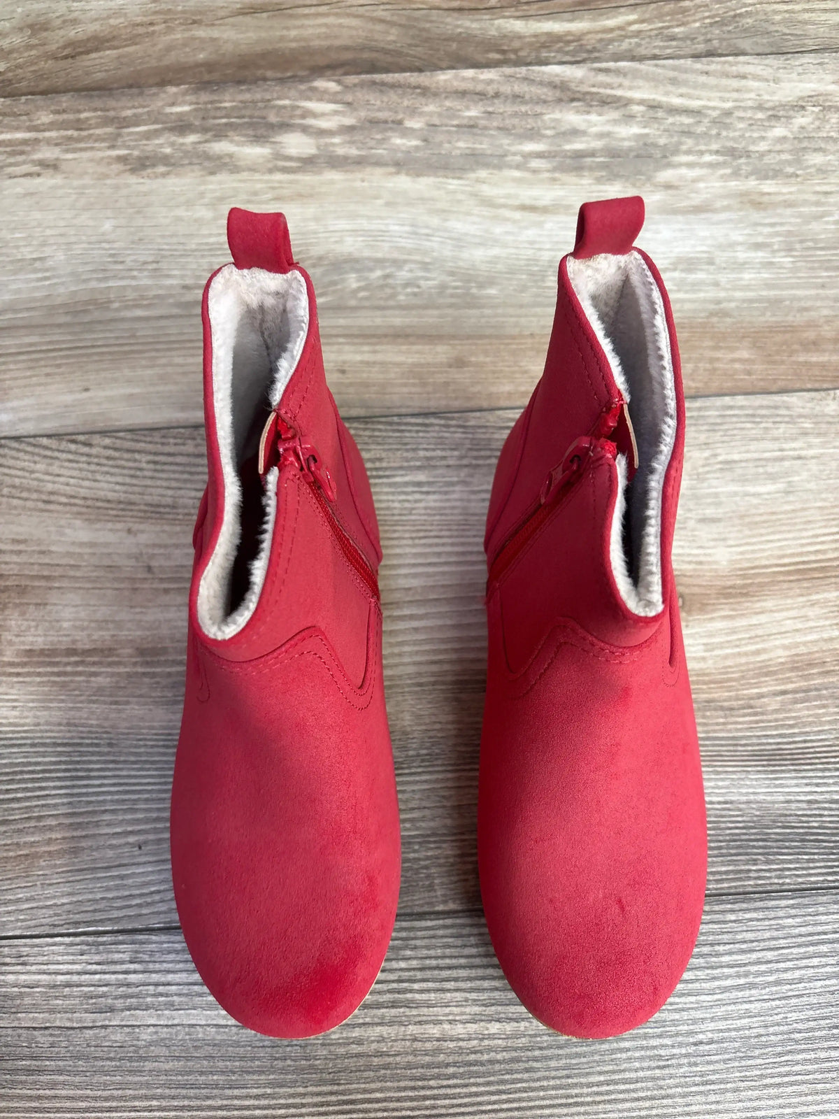 Red suede toddler boots with side zippers and fleece lining on wooden floor
