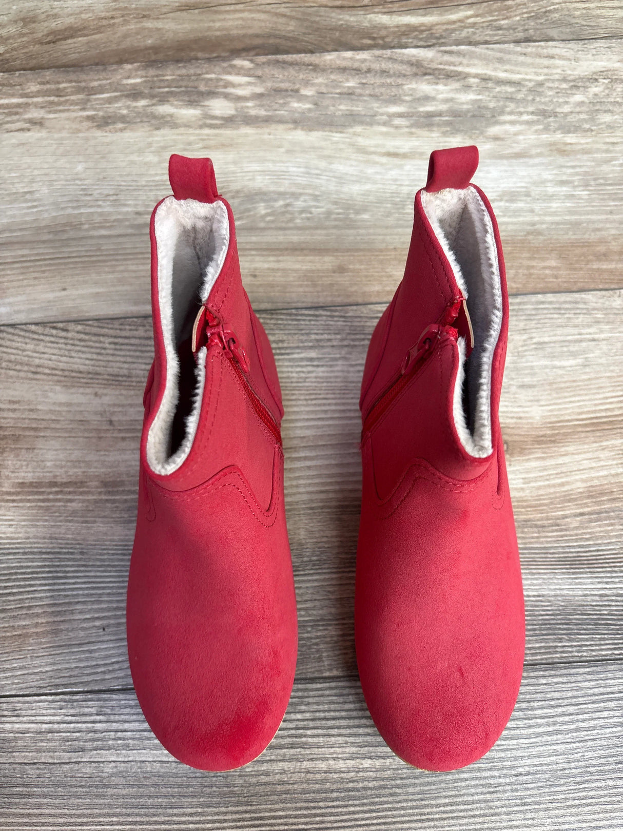 Red suede toddler boots with side zippers and fleece lining on wooden floor
