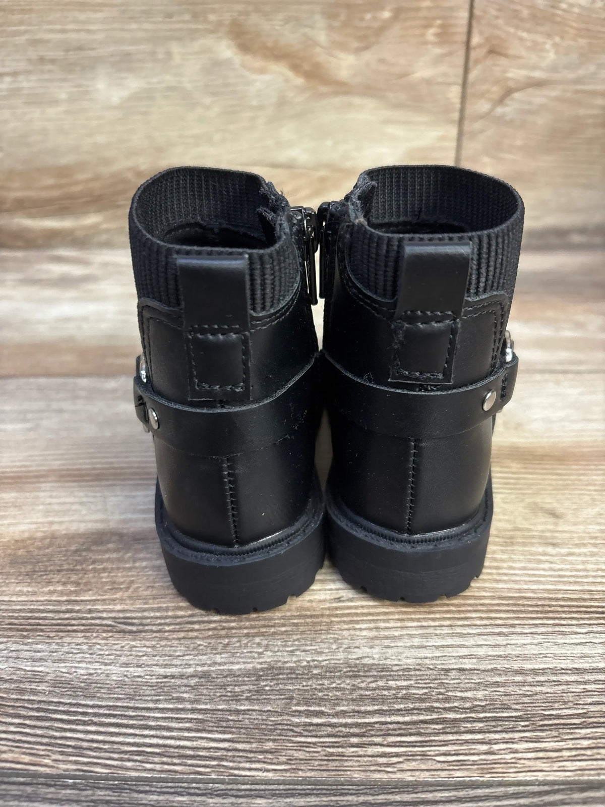 Rear view of toddler black faux-leather moto boots size 6C showing back zipper, elastic ankle cuff and strap on wood floor