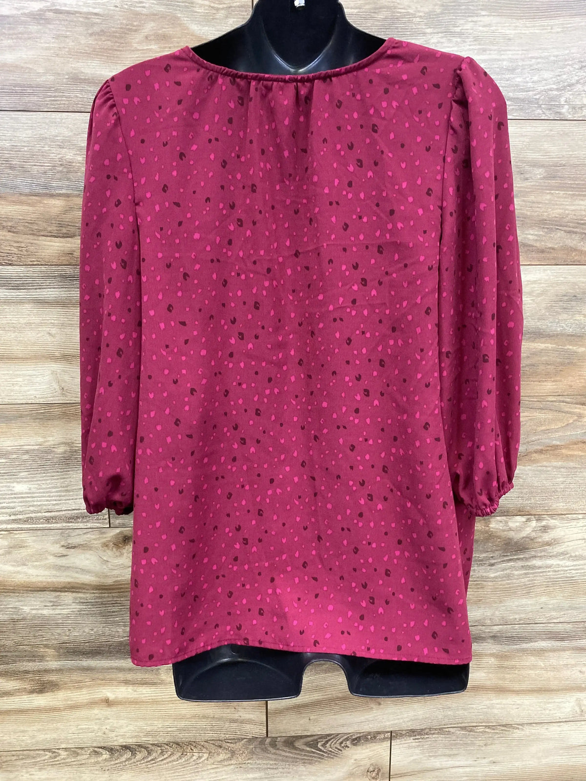 Burgundy long sleeve blouse with pink and black polka dot pattern on wood background
