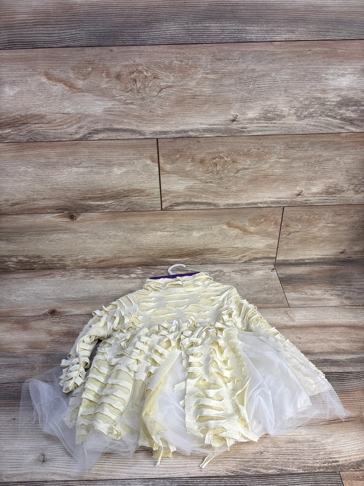 Flat lay of cream toddler mummy costume with wrapped fabric strips, tulle skirt and headpiece on wood background