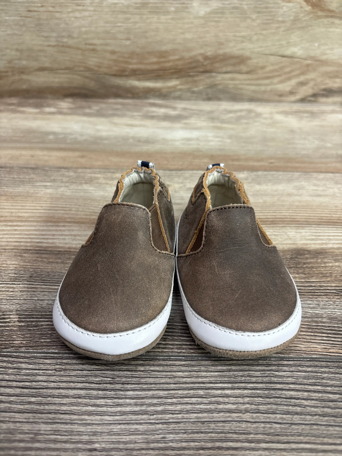 Pair of brown Robeez Lenny Loafer crib shoes for infants on a wooden surface.
