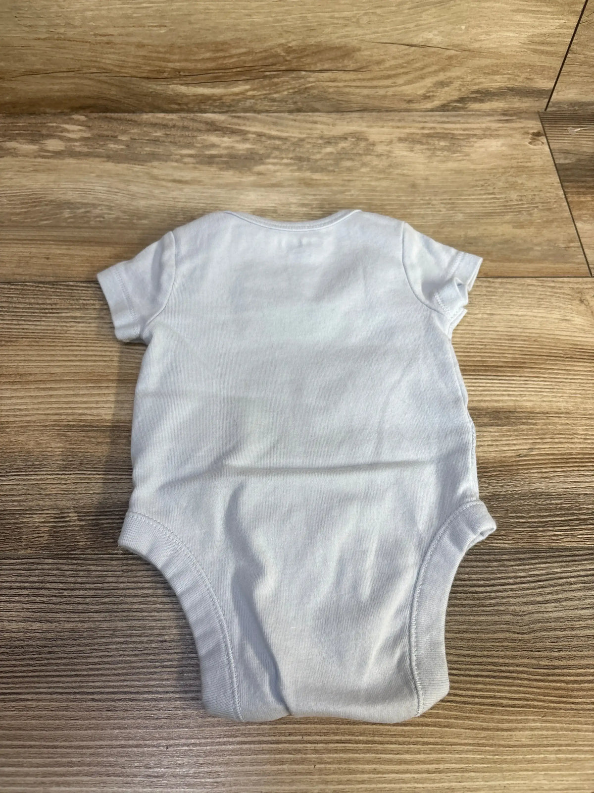 Back view of Old Navy blue bodysuit in size 0 to 3 months showcasing short sleeves on a wood-grain floor